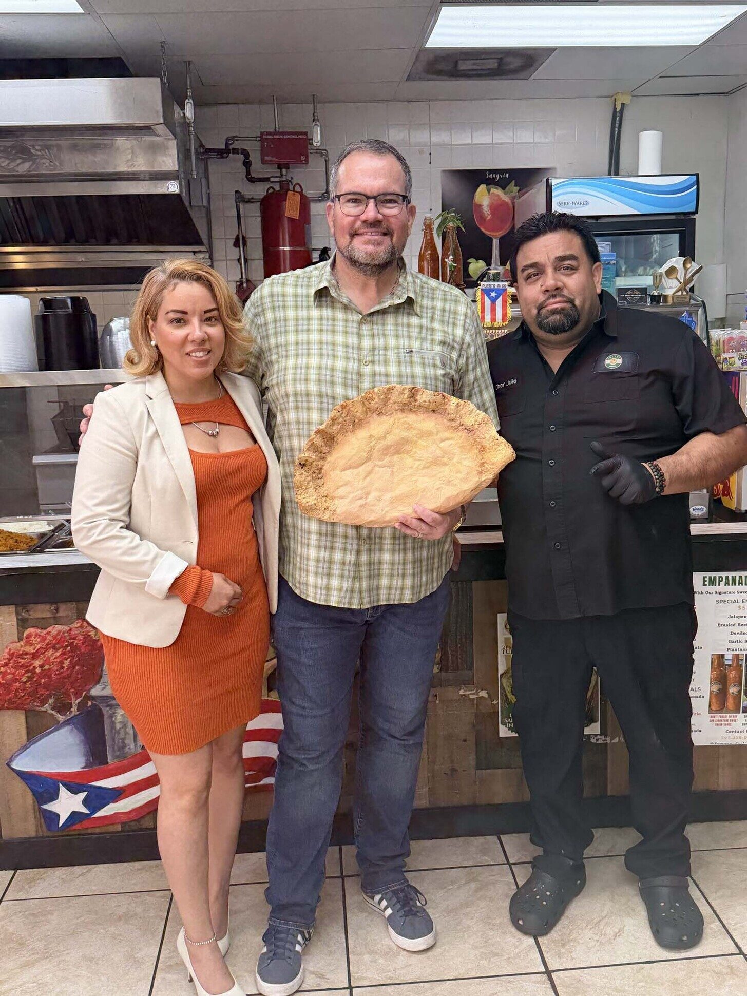Julio and his team in the restaurant kitchen with a giant empanada prop and Puerto Rico flag art on the wall